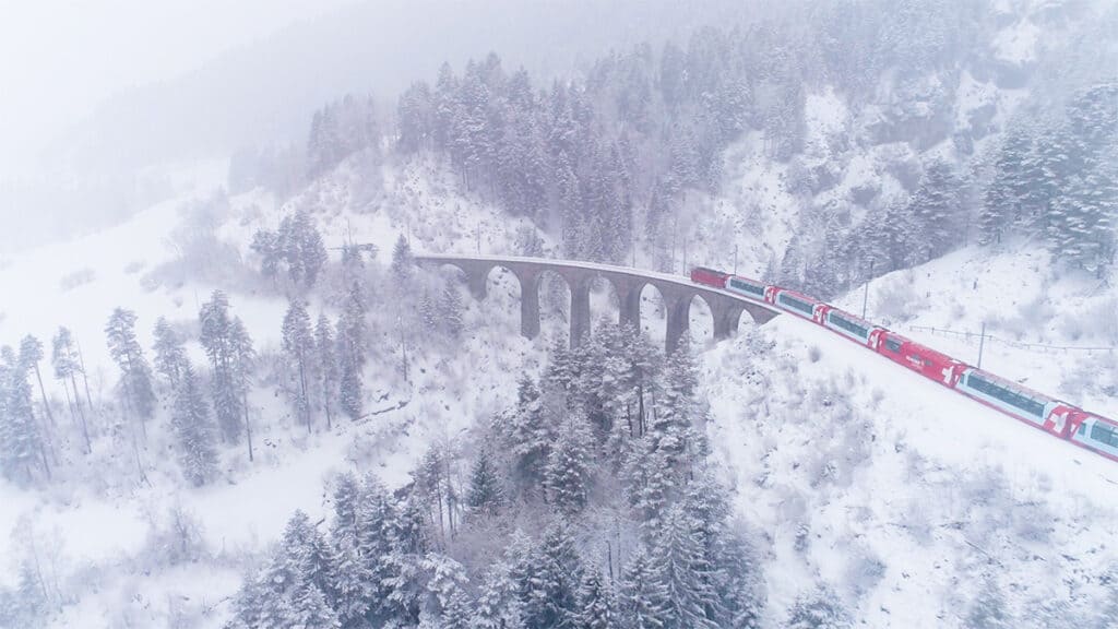 the glacier express train driving through a winter landscape with snow